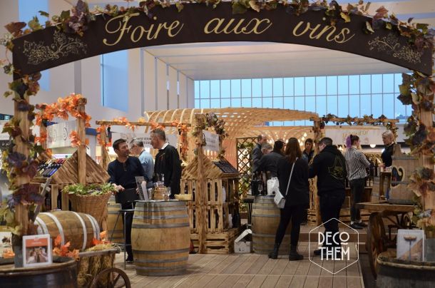 Foire aux vins, portique d'entrée, feuilles de vigne, tonneaux avec plateaux de verre, présentoirs en bois.